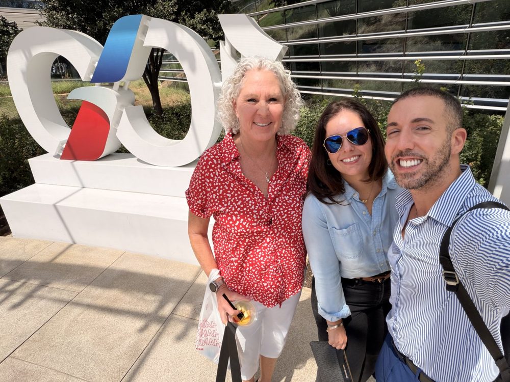 Three community members smiling outdoors at a travel supplier campus